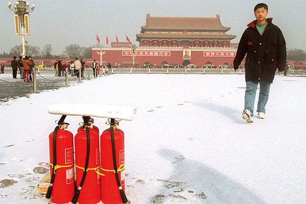 天安門自焚偽案是中共政府策劃的一場騙局，嫁禍法輪功，作為鎮壓的藉口。圖為2001年1月24日自焚偽案隔天，一個便衣上前阻止人照天安門廣場上的滅火器。（Stephen Shaver/AFP）